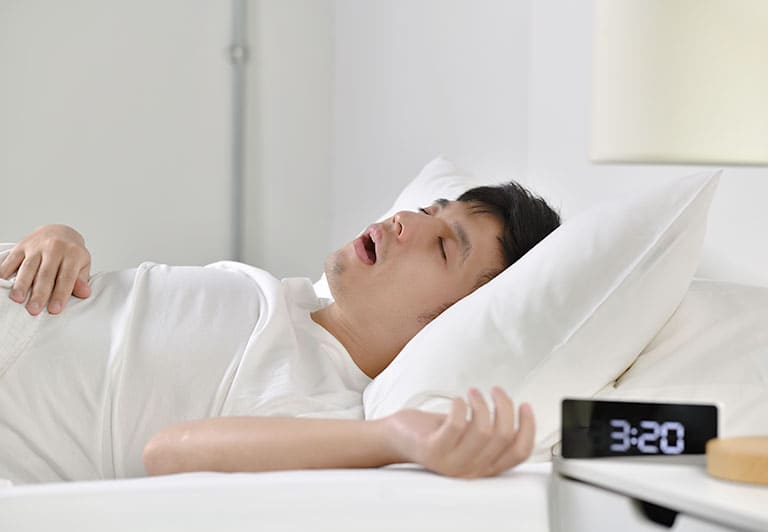 口を開けてベッドで寝る男性