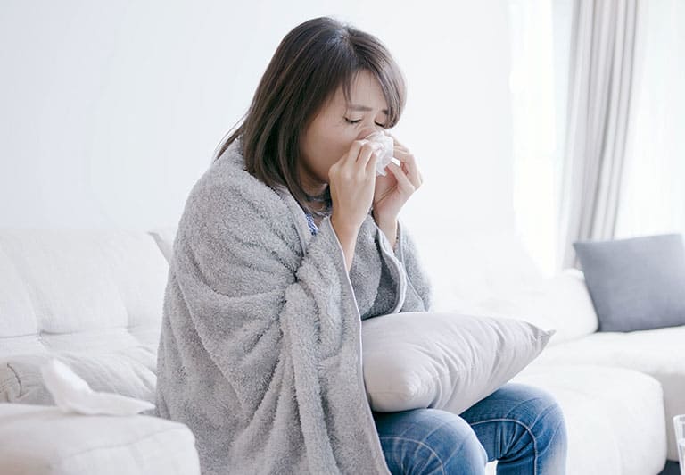 毛布を掛け鼻をティッシュでおさえる女性